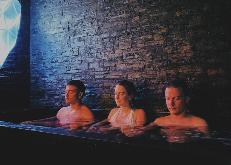 Trois amis en pleine concentration immergés dans le grand bain glacé face au mur de pierre, illustrant l'espace Sōnïce privatisé pour les groupes chez Meisō Olympiades